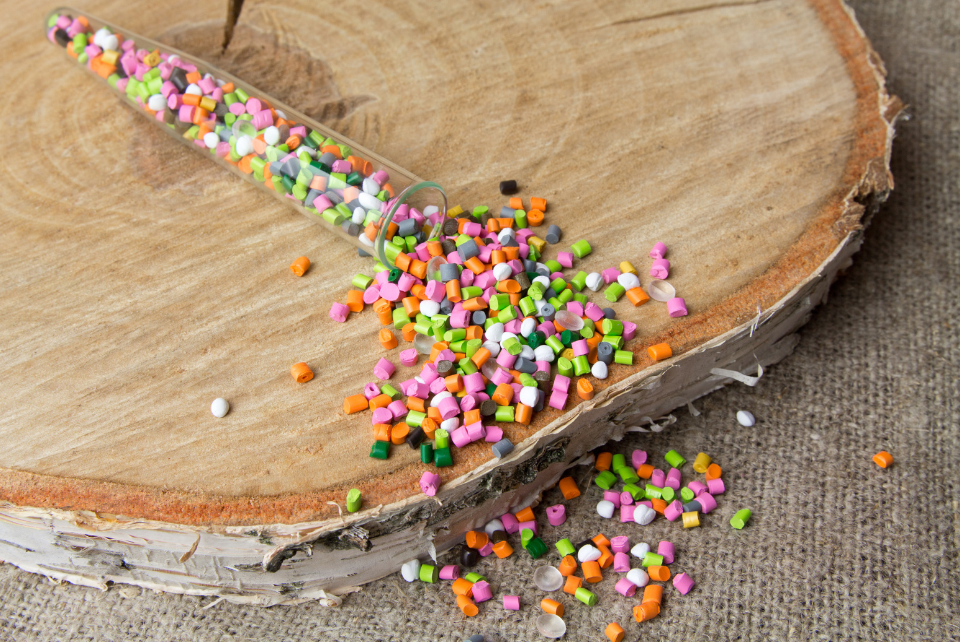 Colorful plastic granules spilling from a test tube onto a wooden surface